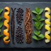Overhead tasting board of tobacco leaves, mint, citrus and berries laid in rows, for choosing an IQOS ILUMA stick