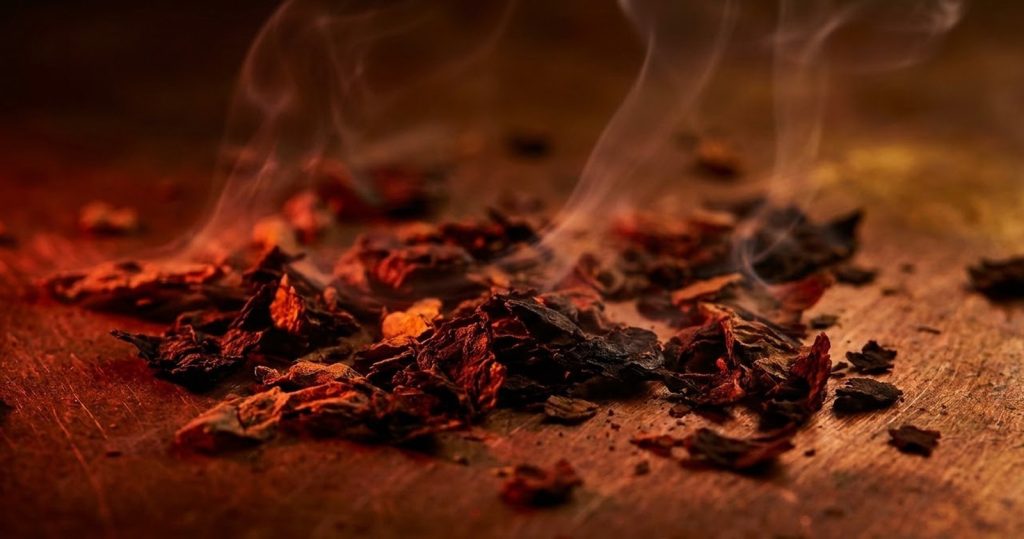 Roasted tobacco leaf on copper with curling smoke, illustrating the NEO stick range for glo Hyper